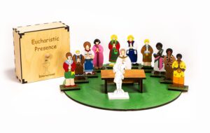 A wooden religious playset titled "Eucharistic Presence" featuring a wooden box and figurines in various traditional attires encircling a white central figure on a green base with a wooden table.
